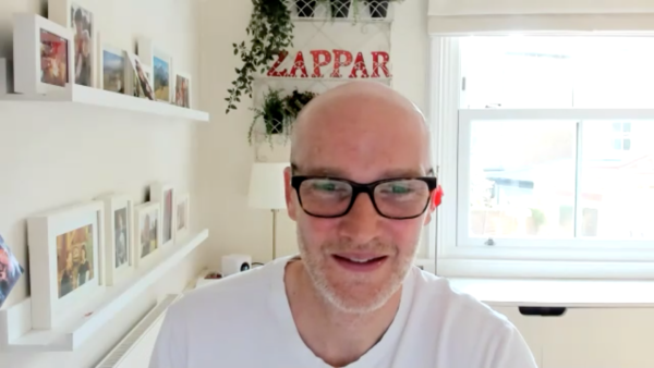 Zappar CEO/Co-Founder Caspar Thykier smiles as he discusses Zappar's latest innovations, with "ZAPPAR" in red lettering in the background