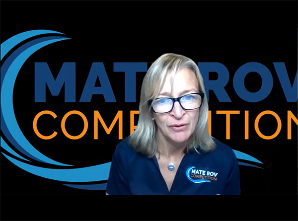 MATE ROV Competition Founder/Executive Director Jill Zande, in a navy blue shirt with "MATE ROV Competition" and a swirling blue wave over the pocket, against a larger background of the same logo.