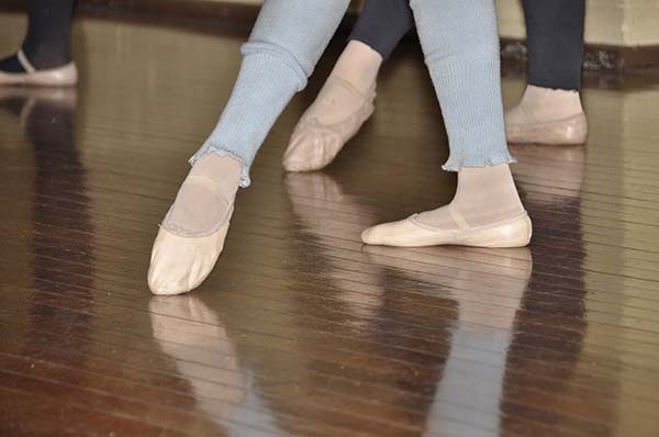 Dancers' legs in blue jeans and feet in leotards and pink dance slippers as they point their feet in a dance position