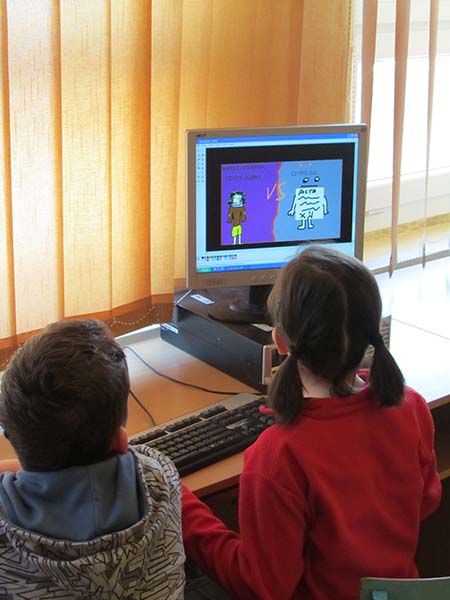Two children--a boy and a girl-- sit facing a computer monitor with cartoon drawing on the screen and a keyboard before them