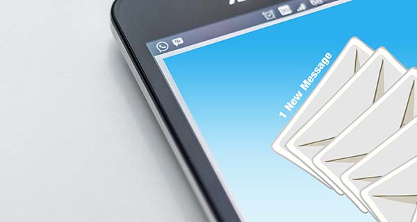 Cell phone on surface with "1 new message" on its screen and graphic of email envelopes.