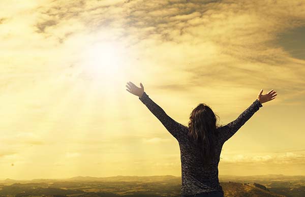 Joyous woman raising her arms to the sun as rays break through the clouds