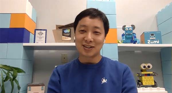 Robolink CEO Hansol Hong, in his startup's teal-blue T-shirt, sits before shelves displaying Robolink's Zumi autonomous-vehicle robot, one of the RokitSmart robots and his CES Innovation Award.