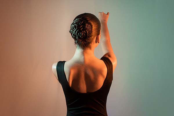 Young woman ballet dancer's back with her hair in a dance bun as she extends her arms.
