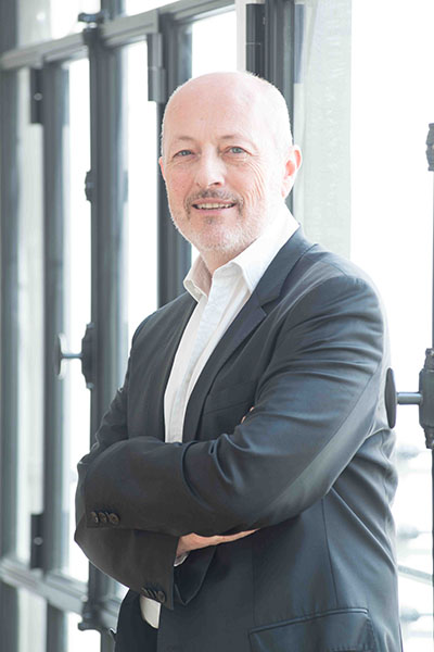 Dr. Bernard Gilly, in a gray suit, near a window in his Paris office