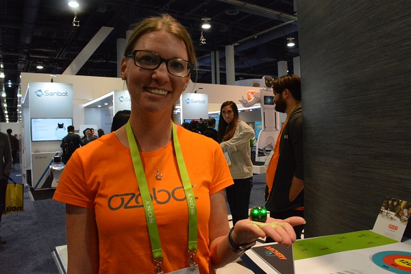 Morgan Andersen in an orange "Ozobot" tshirt, holds a one-inch-tall green Ozobot robot in the palm o f her hand at CES 2018