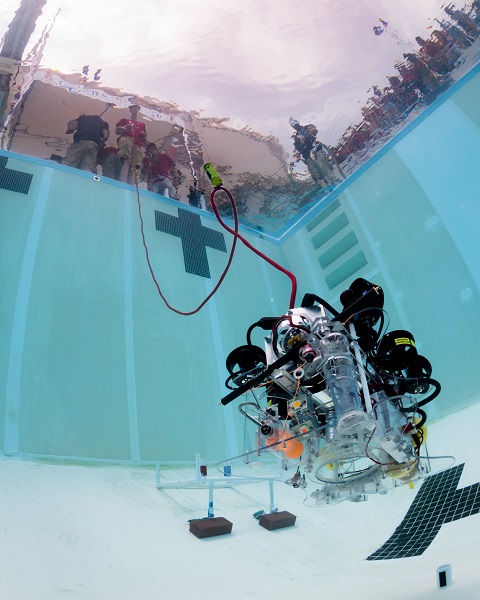 underwater robot navigates the bottom of a pool as robotics competition participants watch