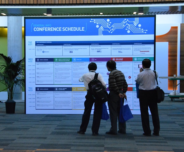 Three Sensors Conference attendees look at a ten-foot printed schedule standing in the main lobby of McEnery Convention Center