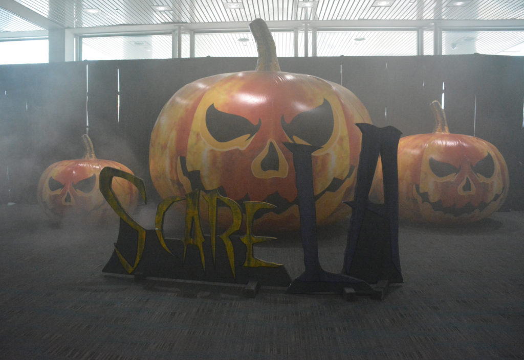 Three pumpkins with "ScareLA" in black in front of them, in fog at entrance to ScareLA 2018
