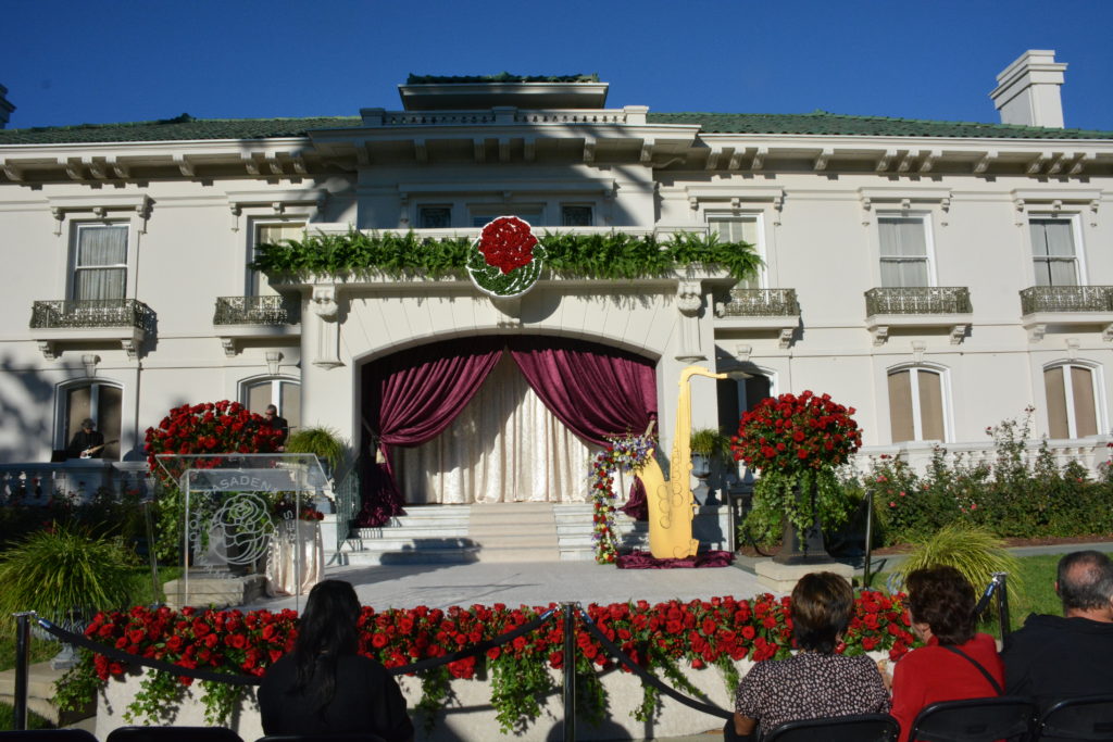 Audience members sit in front of Tournament House decked with rose medallion and purple curtain, prior to Grand Marshal announcement