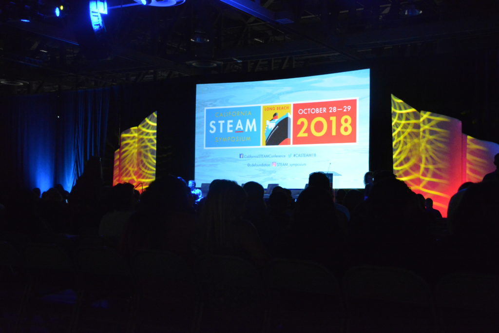 Attendees seated in front of screen with "CA STEAM Symposium 2018"