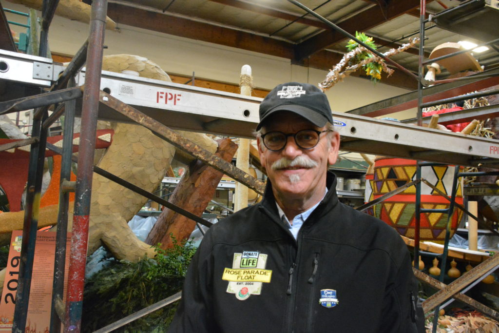 Donate Life Rose Parade float chairman Tom Mone at Fiesta Parade Floats facility next to the 2019 float, "Rhythm of the Heart"