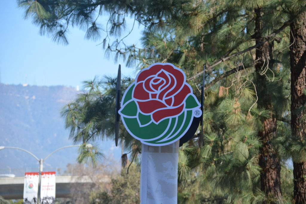 Rose Parade® emblem outside "Decorating Places" location with mountains and trees in the background