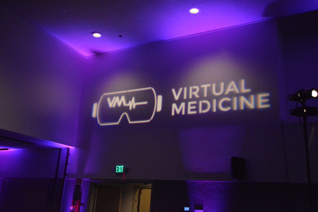 "Virtual Medicine" sign projected in white letters with white headset logo on purple-lit wall