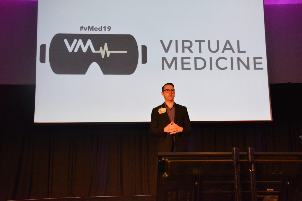Dr. Brennan Spiegel stands onstage before white Virtual Medicine slide at start of Day Two of Virtual Medicine 2019