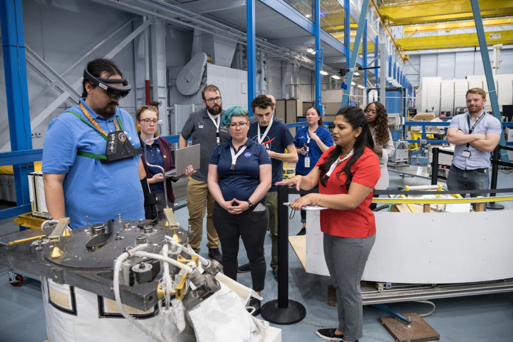 Man wears AR goggles as students participate in NASA SUITS Design Challenge in Kennedy Space Center and woman in red shirt explains technology