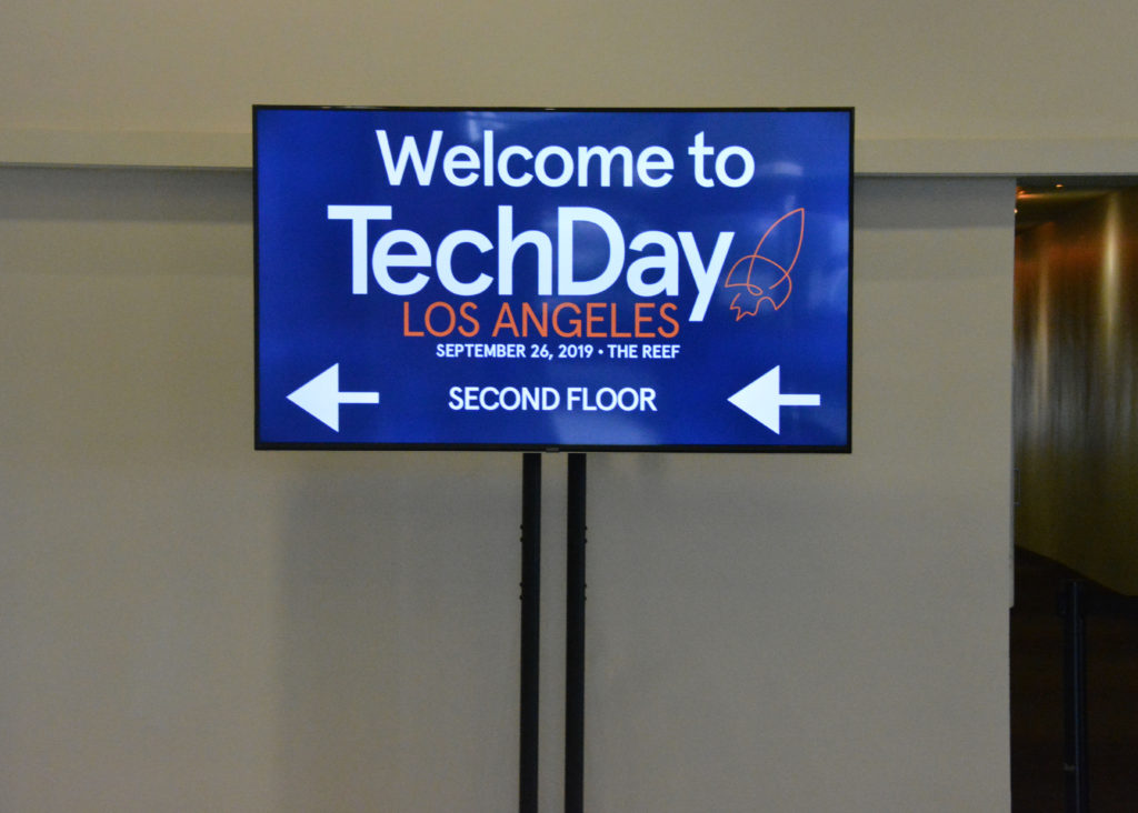 Blue sign in hallway says, "Welcome to TechDay Los Angeles" in white lettering with arrows pointing left