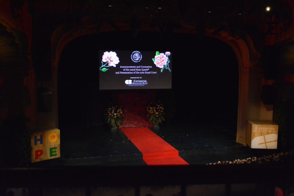 Pasadena Playhouse stage with red carpet and rose-decorated screen with "Coronation of the 102nd Rose Queen", and a block at the side with the word "HOPE" on it
