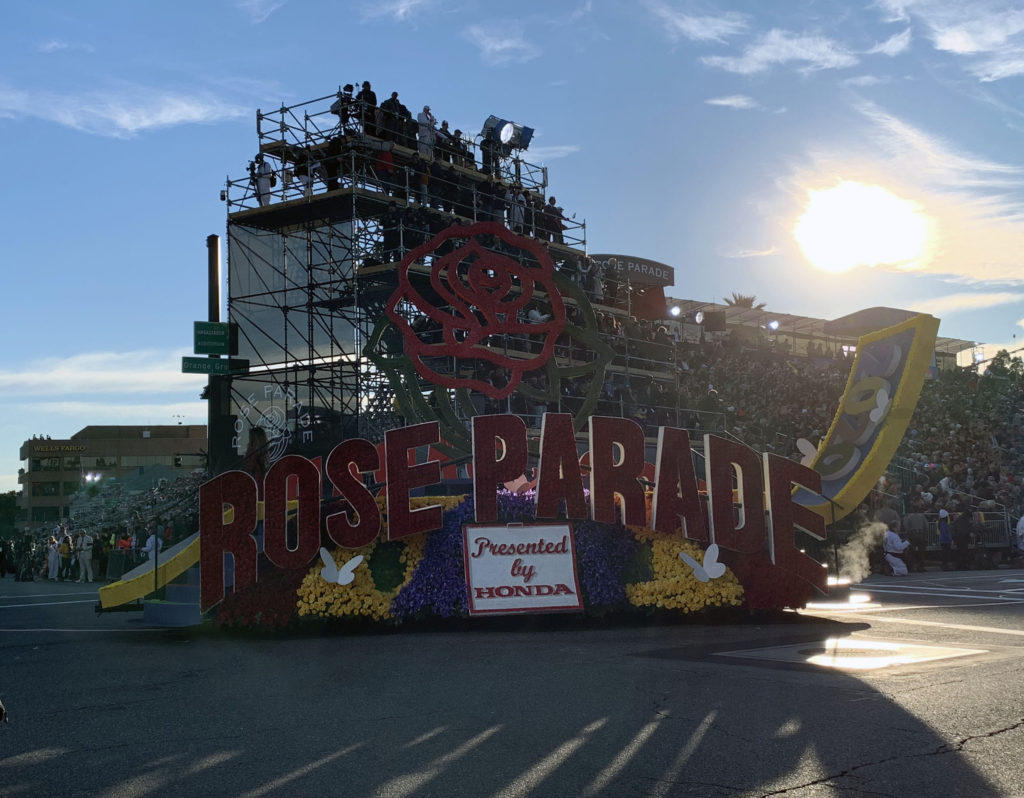 Rose Parade opening float with rose emblem near reviewing stand