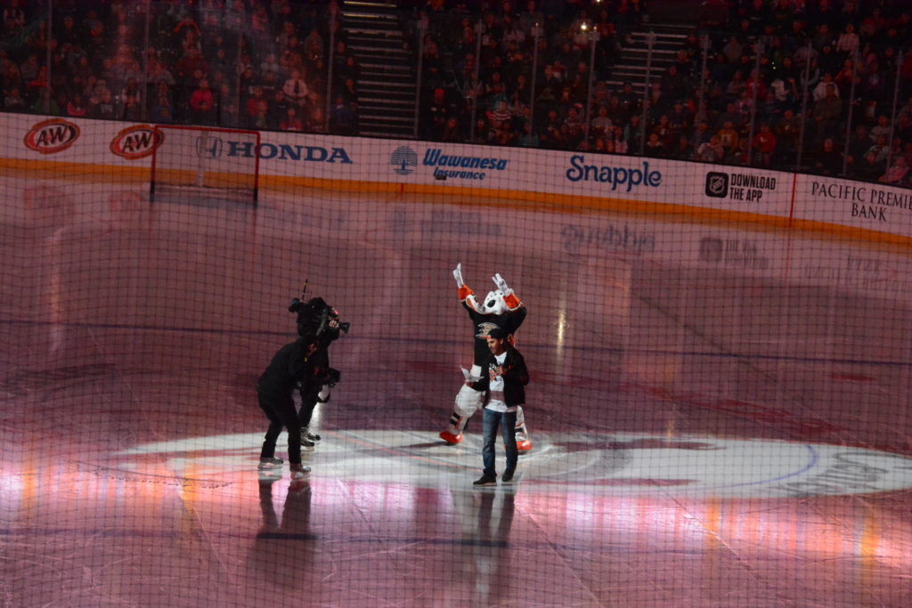 Host Sammy, in skater clothes with dreadlocks, comes onto the ice, accompanied by Ducks mascot Wild Wing