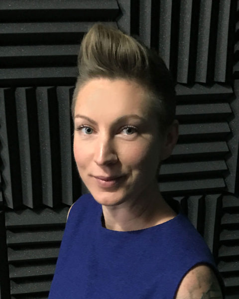 Immersive technology strategist Michelle Excell, in a blue shirt, smiles agains a background of corrugated gray and black fabric