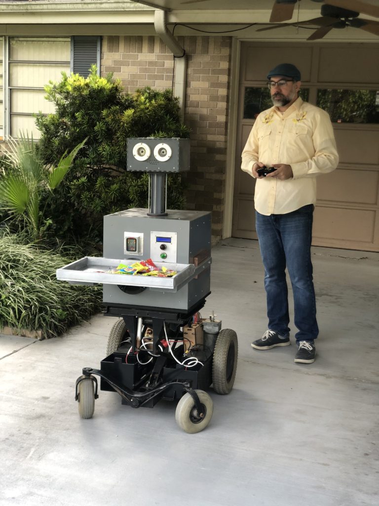 Roboticist Luke Keyes controls "Artie" robot from hand controller as Artie wheels forward with a tray of candy