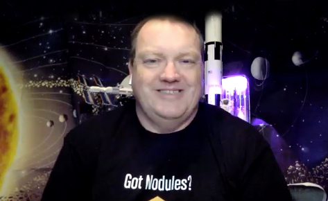 "Space Teacher" Steve Jones in a black T-shirt with "Got Nodules?" on it, against a background with a rocket on a launch pad