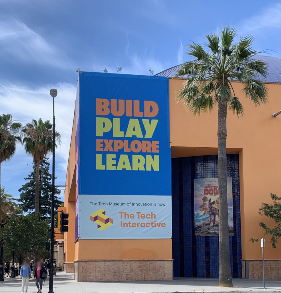 The Tech exterior with palm tree and blue banner that says, "Build, Play, Explore, Learn".