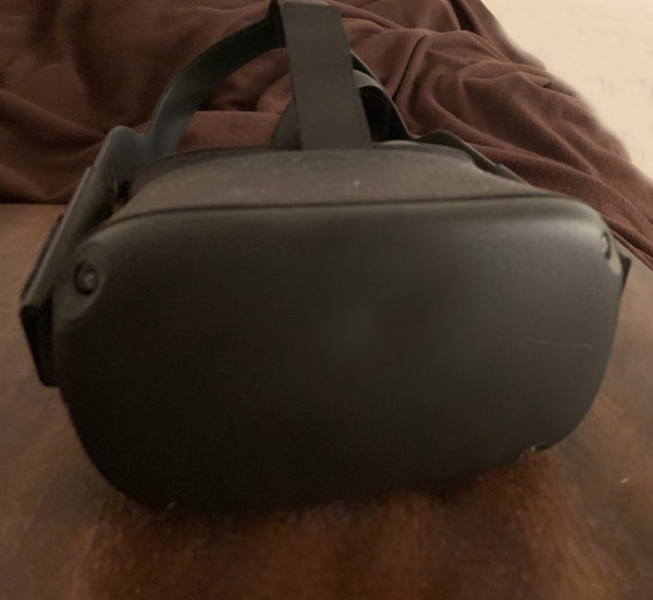 Black Oculus Quest headset on a brown wooden table with a brown blanket in the background