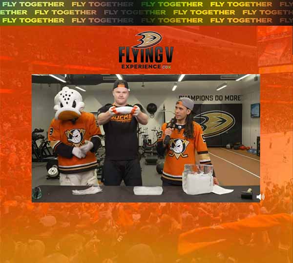 Ducks forward Max Jones holds up a cloudy solid piece of ice while flanked by Ducks mascot WIld Wing and First Flight host Samy Maldonado in Ducks locker room