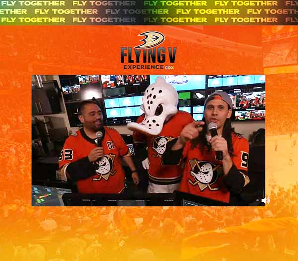 Sammy and Jojo, with mics in hand, stand with Wild Wing in front of a bank of TV monitors