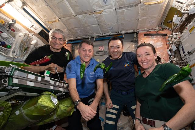 Astronauts aboard the ISS smile as a pepper floats before them in space