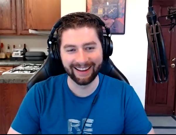 REM5 Lead Developer Matt Foreman, in a blue Tshirt, smiles against a Zoom background of a kitchen setting.