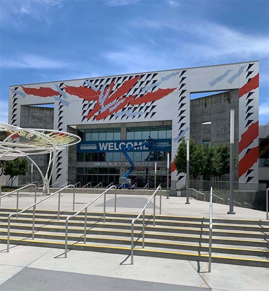 Blue crane lifts blue banner with "Welcome Sensors Expo" onto front of McEnery Convention Center