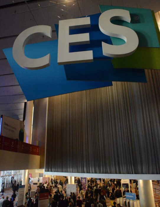 CES sign from underneath perspective, with CES conference attendees milling about the lower floor at the foot of the escalator