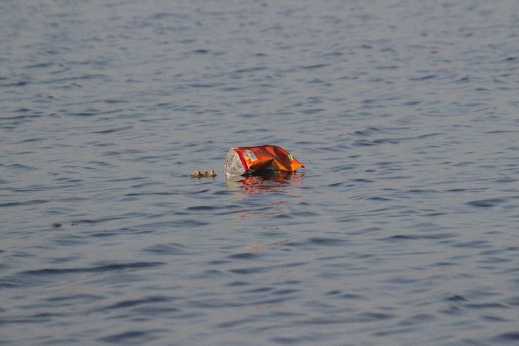 A discarded red plastic container floats in gray ocean water