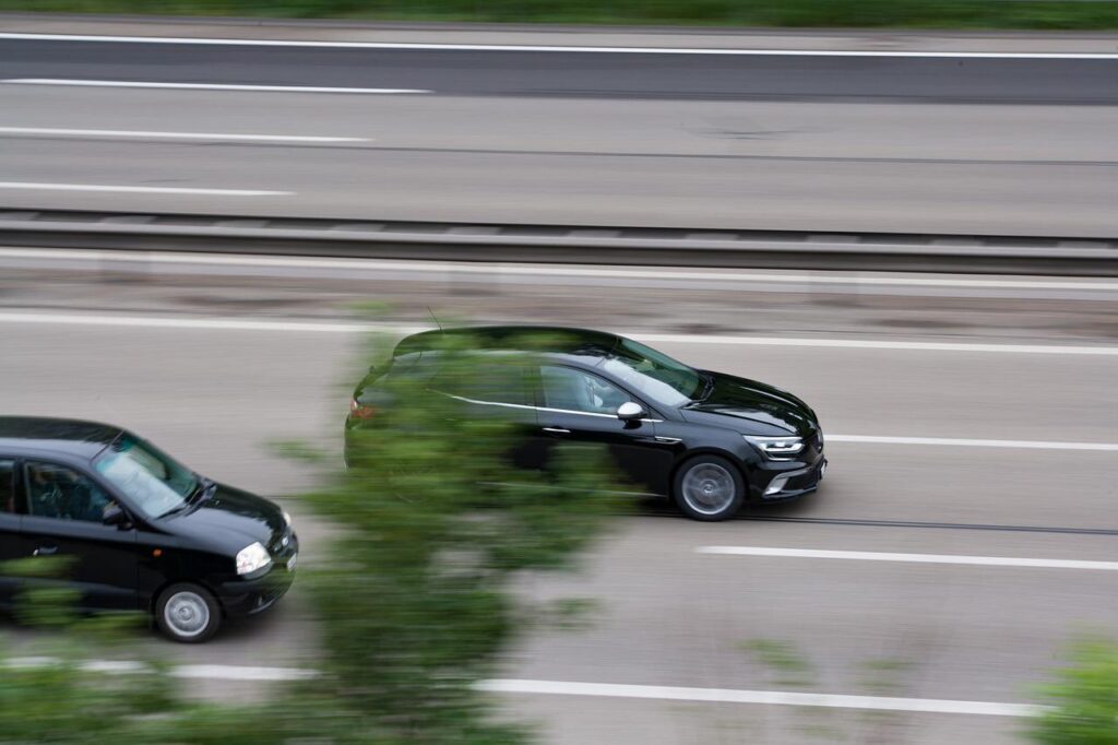 Black autonomous vehicle speeds past another black autonomous vehcile on a freeway