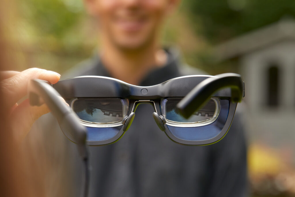 Pair of smart glasses from wearer's perspective with smiling blurred man in the background