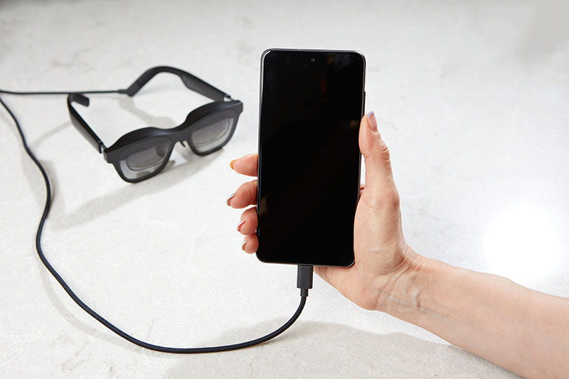 A hand holding smartphone connected to smart glasses by a cable