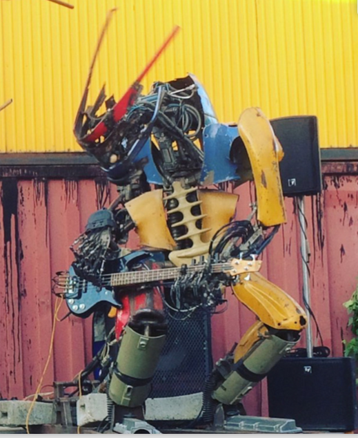 Robotic bass player with red metal "braids" strikes a commanding pose as he plays a light-blue bass.