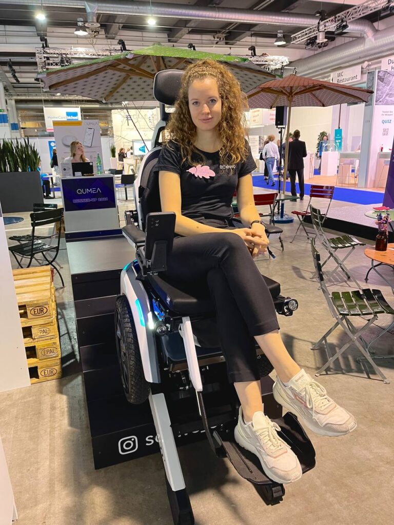 Scewo Lead Communications and Public Relations Manager Natalie Rotschi poses on the Scewo wheelchair on a conference floor