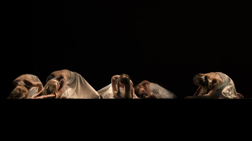 Troupe of dancers in white stretch into dance poses onstage.