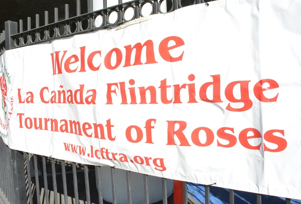 White banner with "Welcome" and "La Canada Flintridge Tournament of Roses" in red lettering on black fence