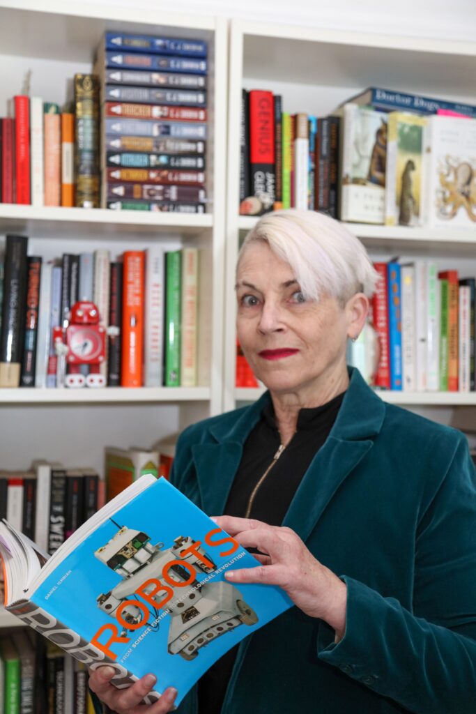 Silicon Valley Robotics Managing Director Andra Keay holds a "Robots" picturs book as she stands near bookshelves filled with colorful volumes