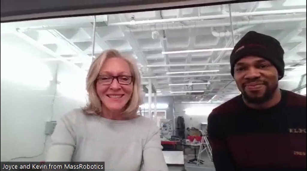Joyce Sidopoulos and Kevin Smith of RoboBoston smile against the background of their robotics lab while discussing RoboBoston.