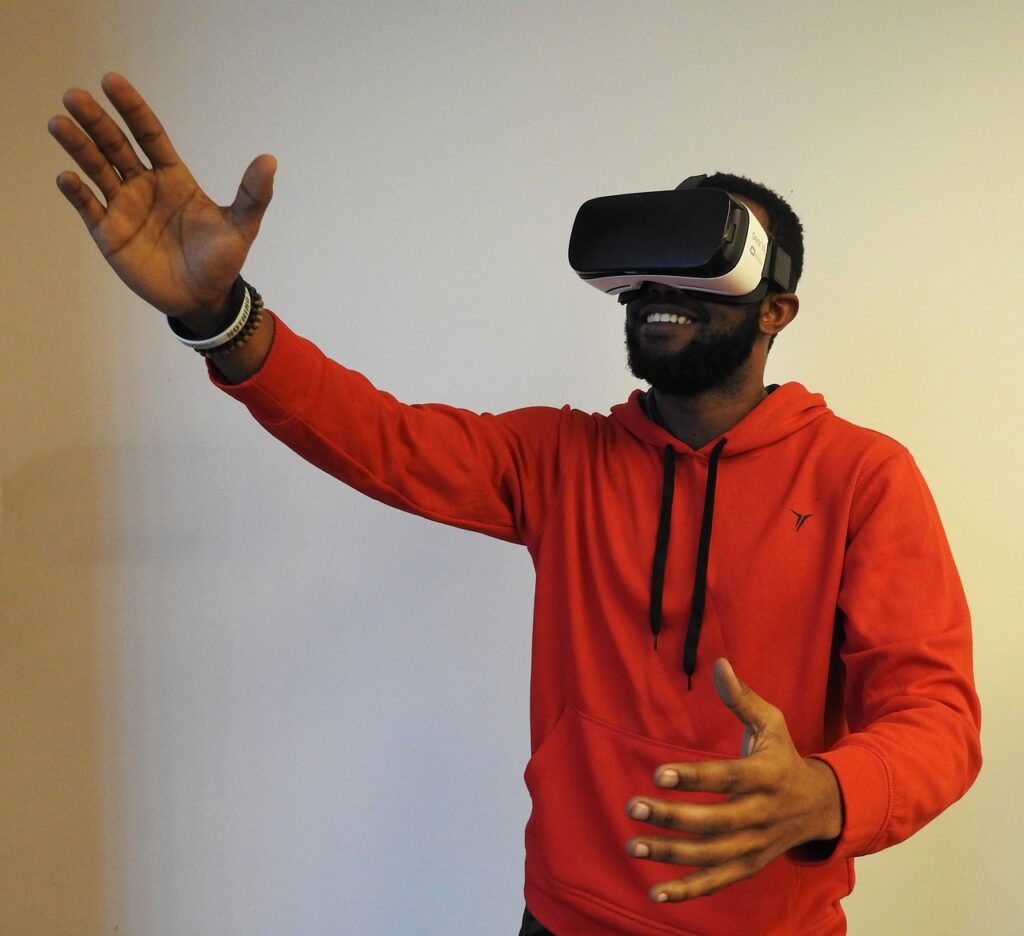 Man in orange hoodie and VR headset smiles as he reaches up an arm for something in front of him in the virtual world.