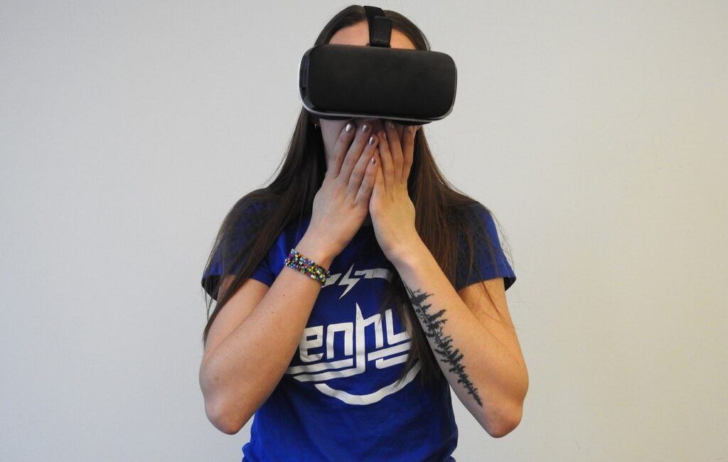 Woman in a black T-shirt and VR headset claps her hands over her mouth in amazement.