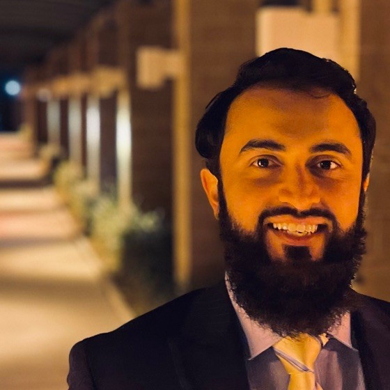 BeAware Founder Saamer Mansoor smiles against the background of a university building at night.