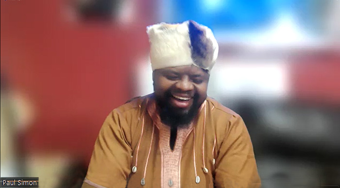 Africa VR Campus and Center Founder/CEO Paul Simon Waiyaki, in a tan African tunic trimmed with white shells and a black-and-white fur turban, smiles as he discusses his nonprofit's VR programs.