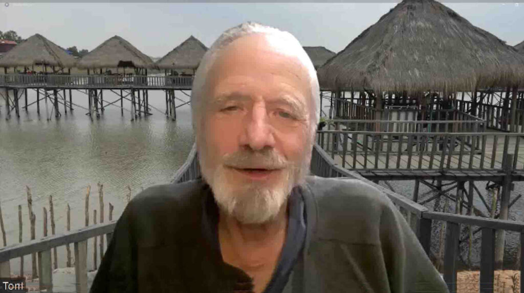 Africa VR Campus and Center Co-Founder and Associate Director Tom Nickel smiles against a Zoom background of a Cambodian village.